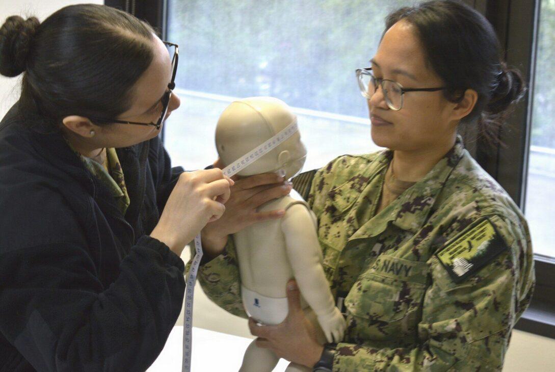 Two women practice infant cpr on a dummy.