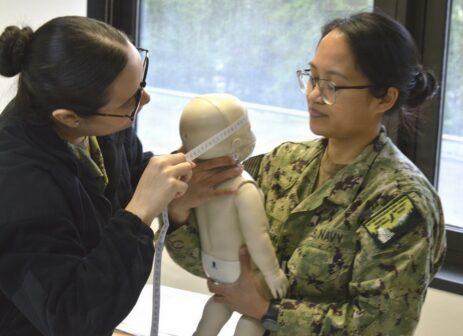 Two women practice infant cpr on a dummy.