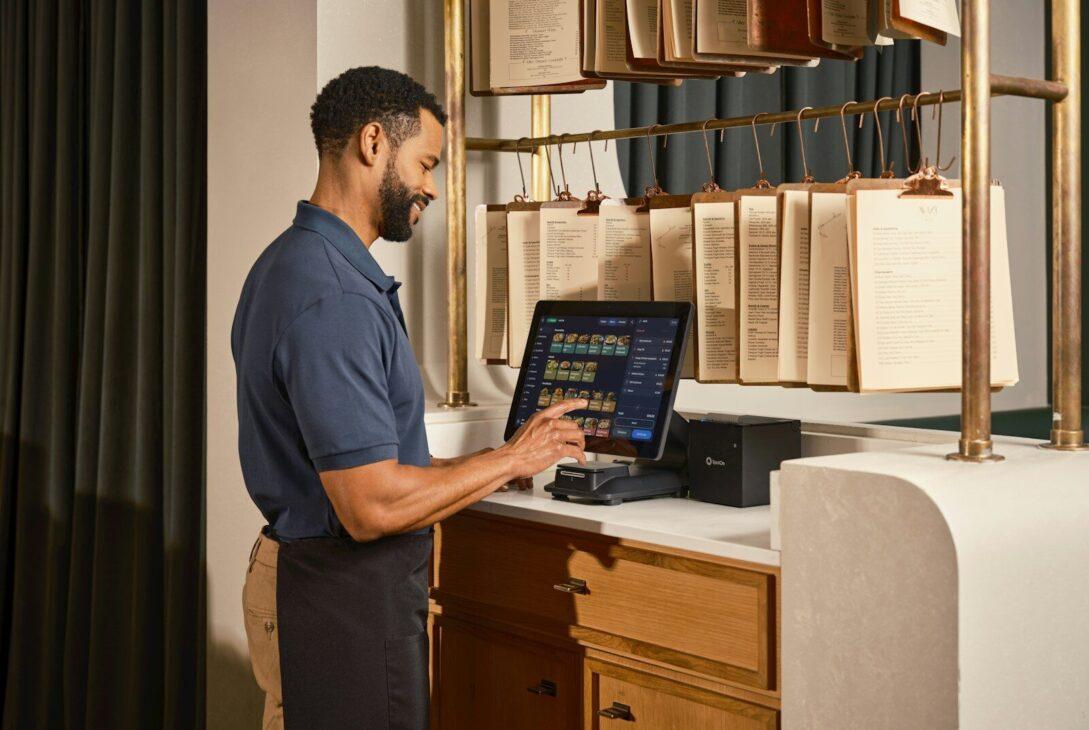 Smiling man operates a point-of-sale system at a stylish counter.