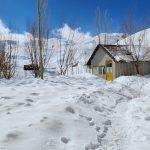 a snow covered road with a small house in the background