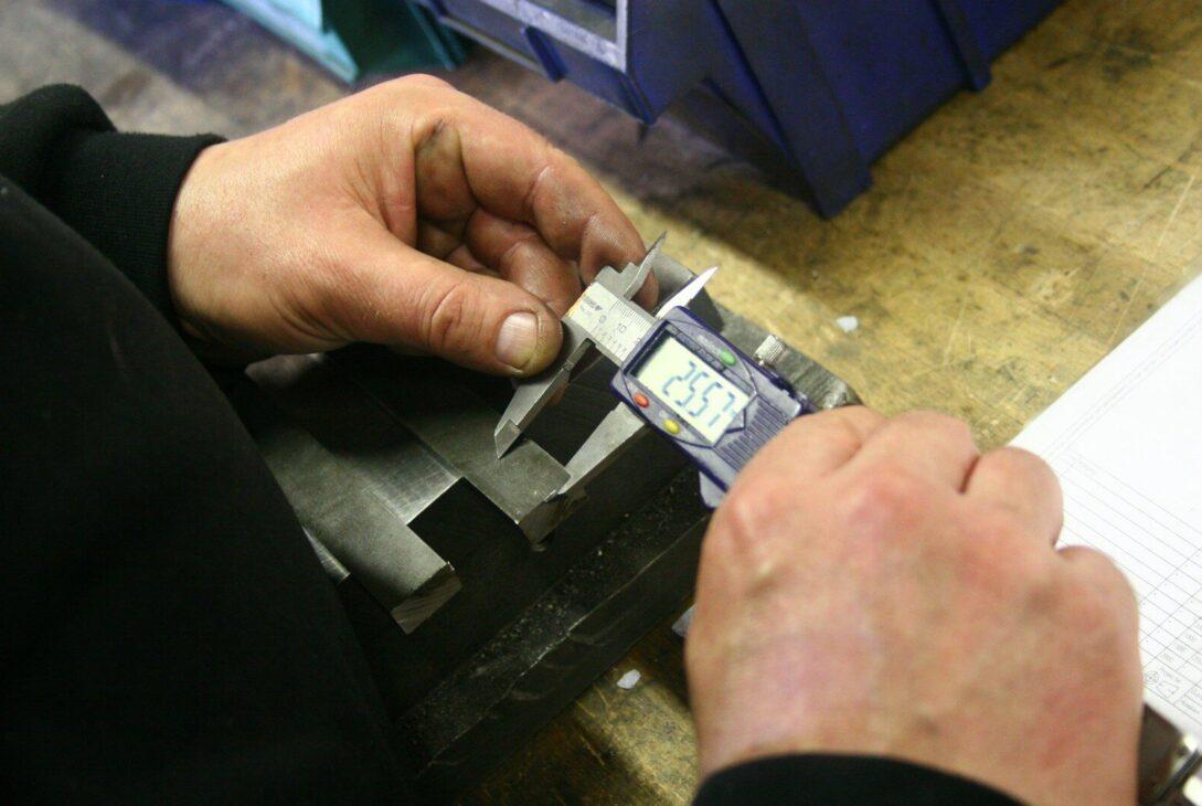 Hands using a digital caliper to measure metal part.