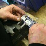 Hands using a digital caliper to measure metal part.