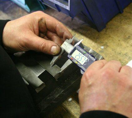 Hands using a digital caliper to measure metal part.
