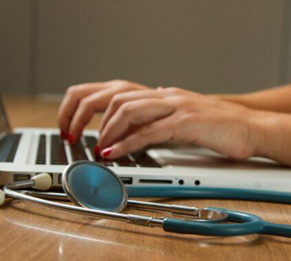 person sitting while using laptop computer and green stethoscope near
