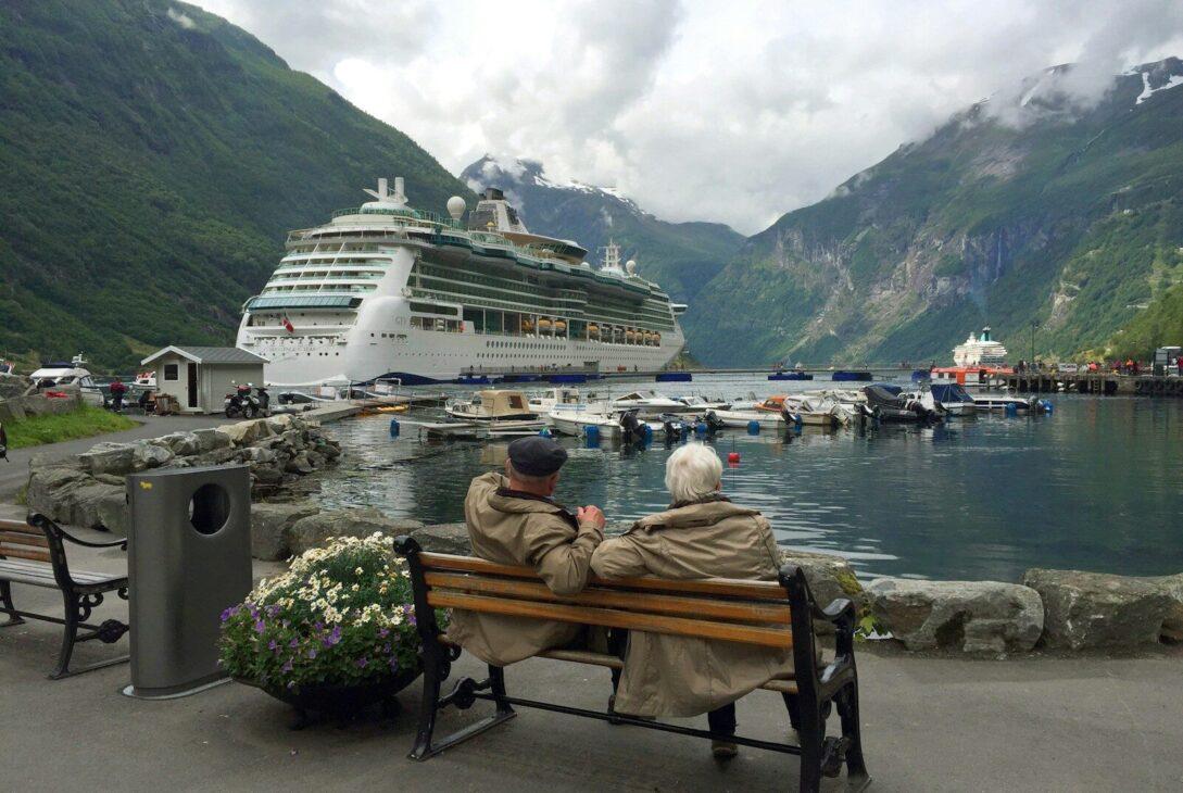 woman in brown coat sitting on brown wooden bench near white cruise ship during daytime