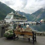 woman in brown coat sitting on brown wooden bench near white cruise ship during daytime