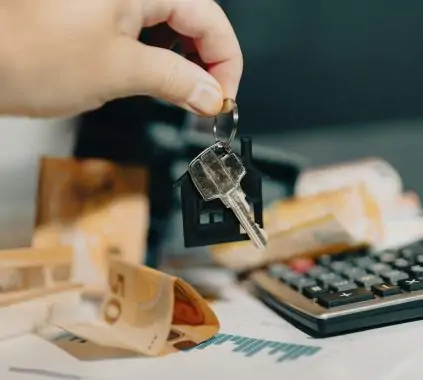 A person holding a house key in front of a calculator